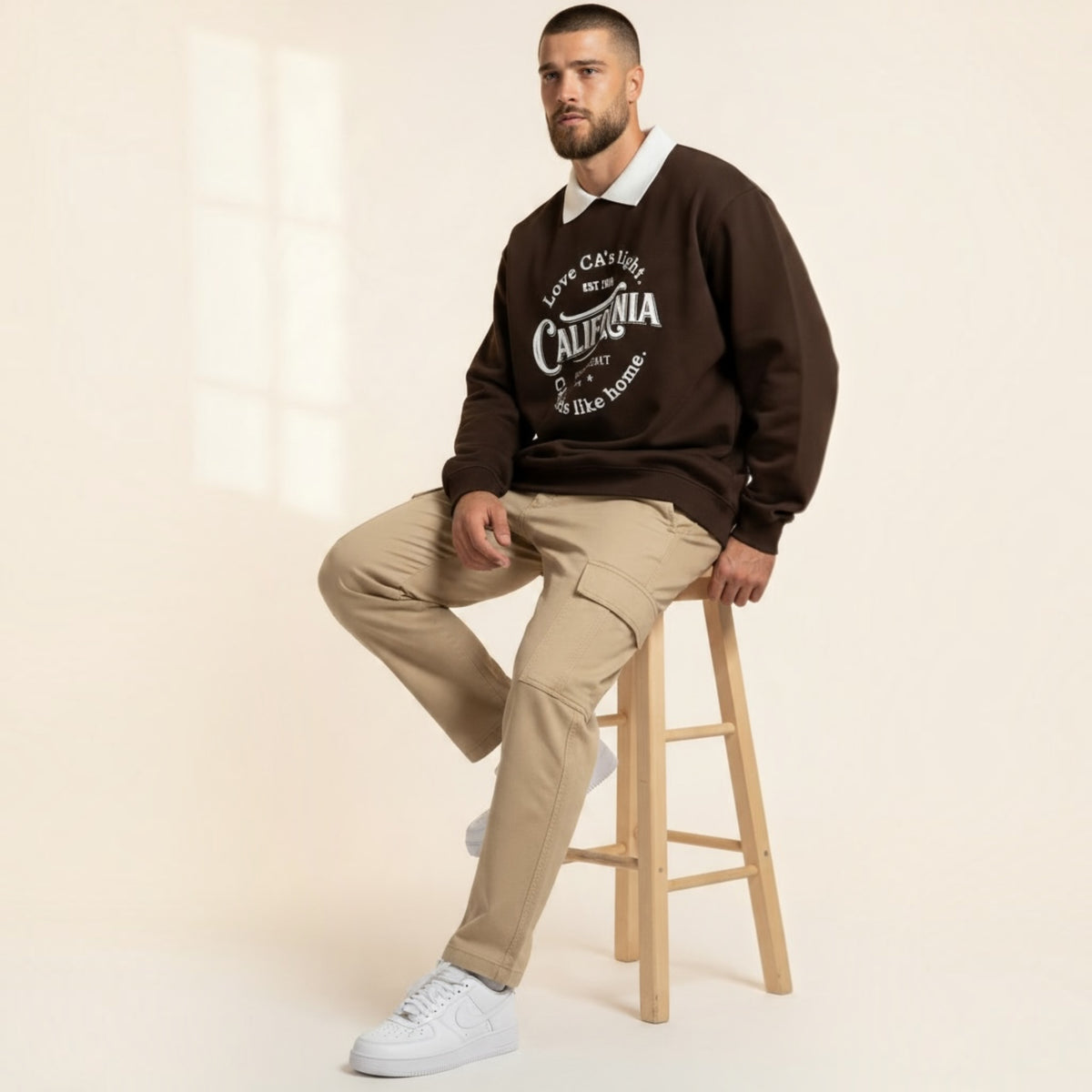 Modello Chulo Store indossa felpa marrone girocollo con colletto bianco a contrasto e grafica California su sgabello
