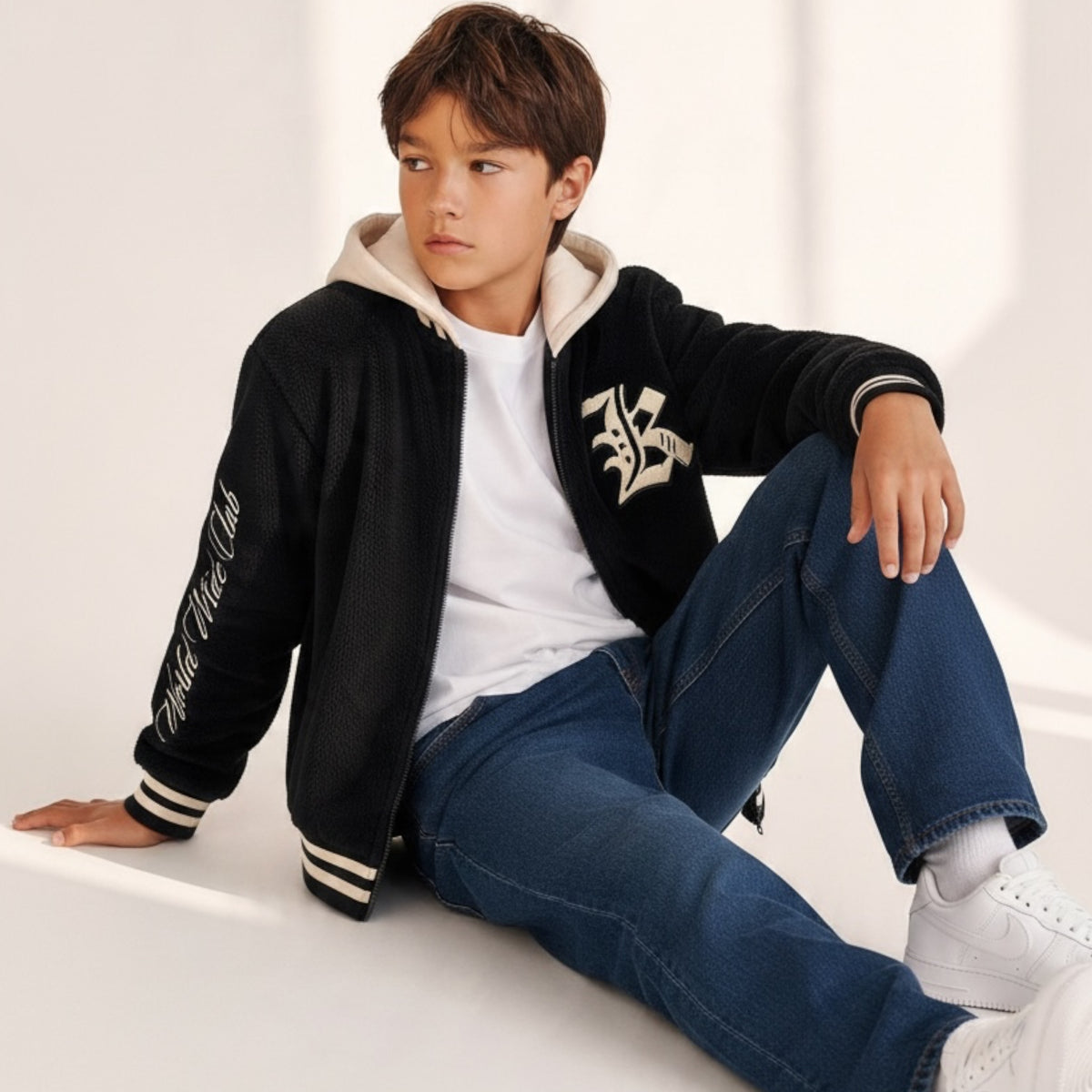 Ragazzo indossa giacca bomber Chulo Store nera in pile con cappuccio crema, scritta World Wide Club e dettagli a coste