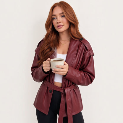 Modella con giacca Chulo Store in ecopelle bordeaux con cintura in vita e spalline strutturate, stile casual chic.