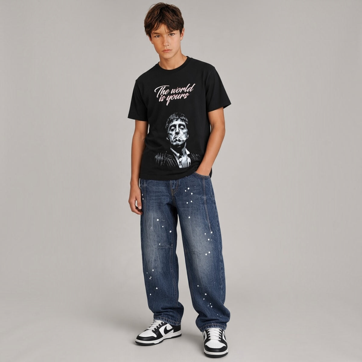 Ragazzo indossa jeans Chulo Store baggy blu con macchie di vernice bianca, t-shirt nera e sneakers streetwear