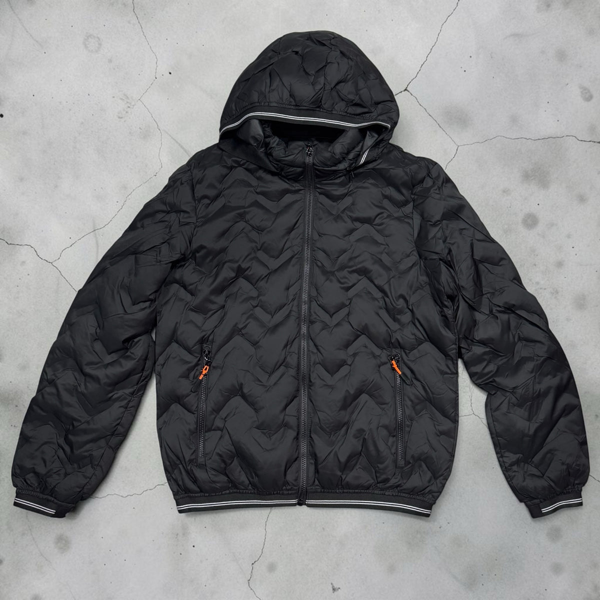 Piumino nero Chulo Store con cappuccio, trapuntatura a onde, zip arancioni e finiture a righe su polsini e fondo.